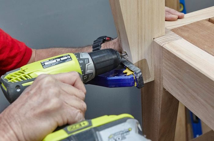 Backrests being attached to a wooden chair with a power drill, while a clamp holds it in place