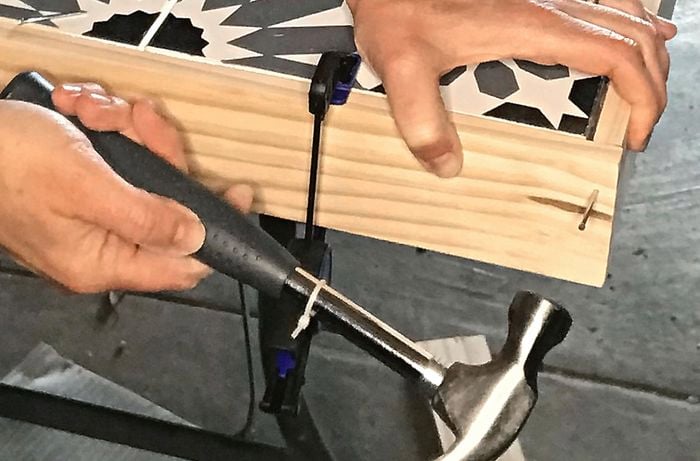 A person hammers pine frames to a tiled table