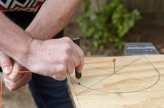 A person drawing a circle on plywood using a string attached to a screw