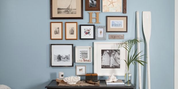 A blue wall with many frames pictures and prints hanging on it