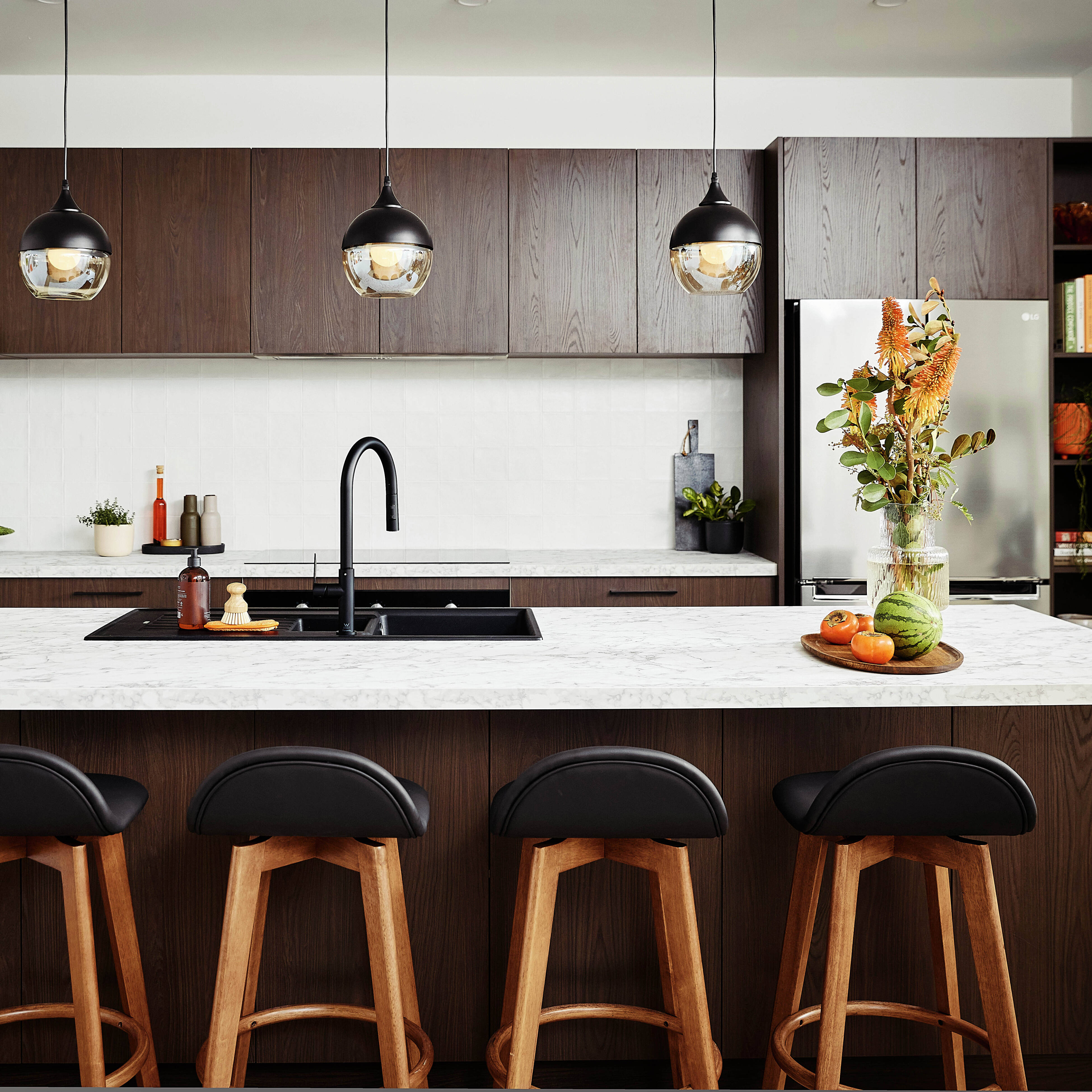 Brown modern kitchen with a white marble benchtop and back bar stools at the bench.