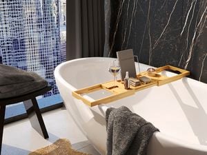 Bathroom with bathtub along with wooden bath caddy, towels and black design wall tiles.