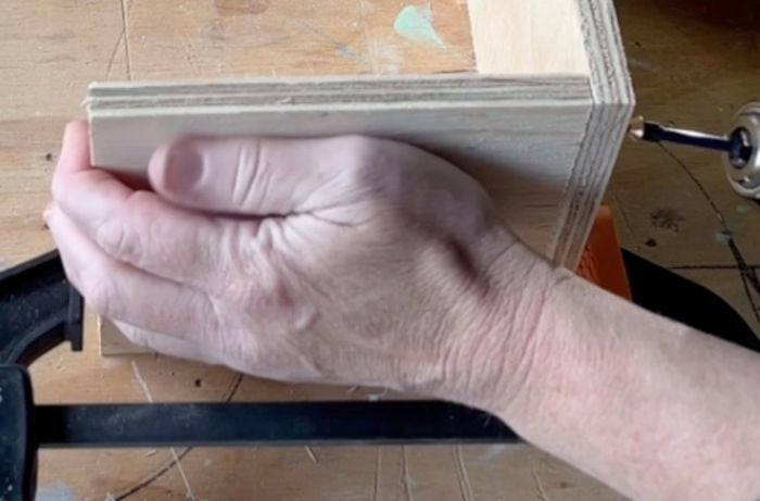 Hands attaching two, upright pieces of plywood together at a 90 degree angle.