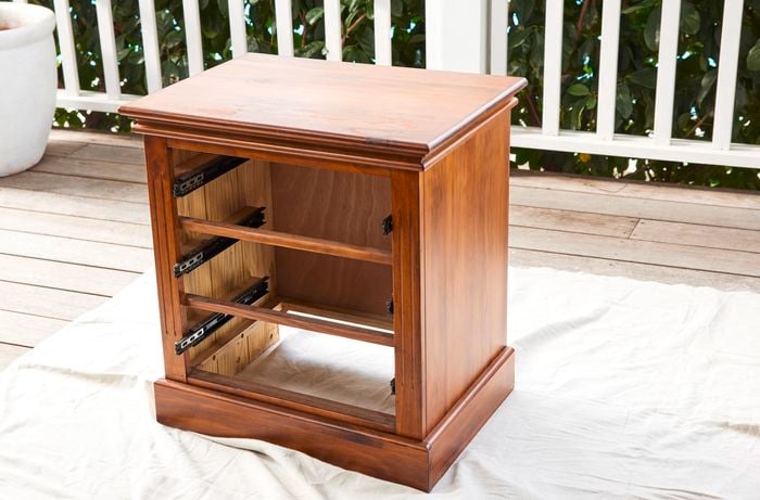 Wooden bedside table with drawers removed, outside on a drop sheet.