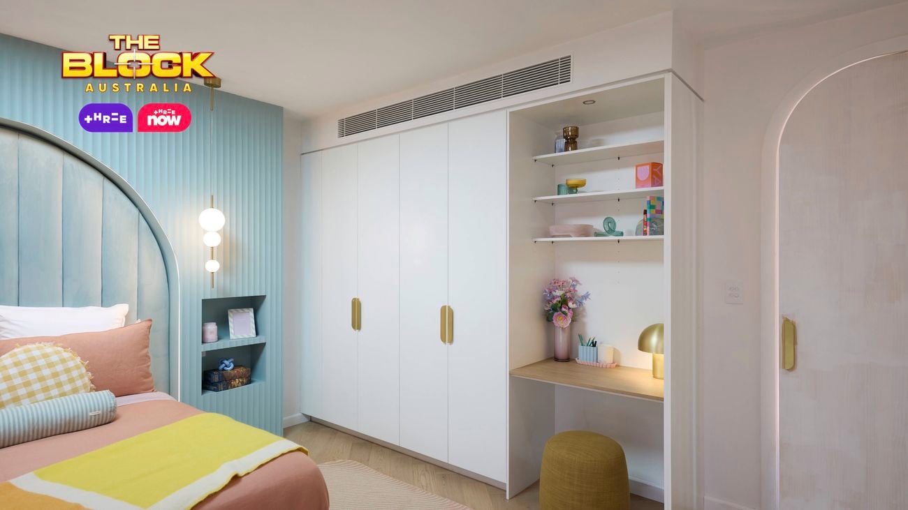 Pastel bedroom featuring a pale blue feature wall with recessed bedside tables and a wardrobe and desk.