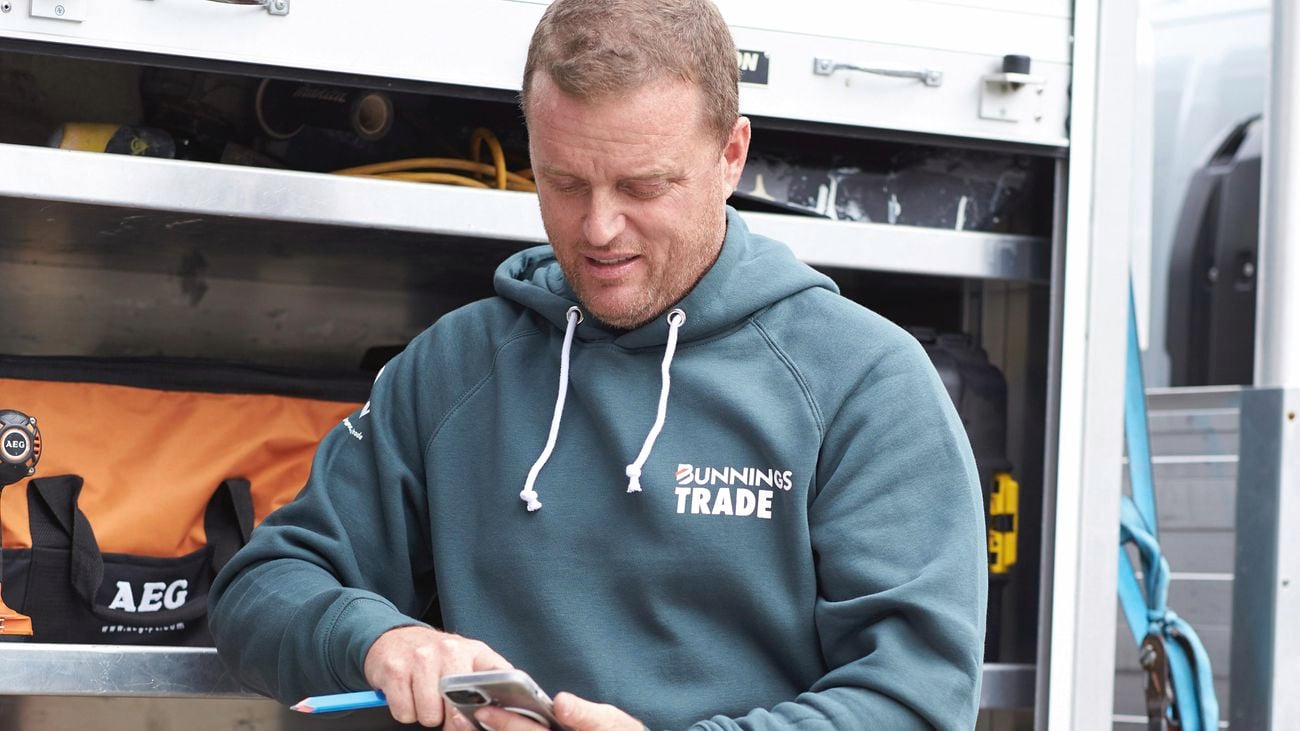 Man leaning against his truck with the boot open looking at his mobile phone