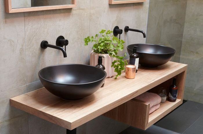 Two black ceramic bowl basins on a floating timber vanity in a bathroom with slate floor tiles