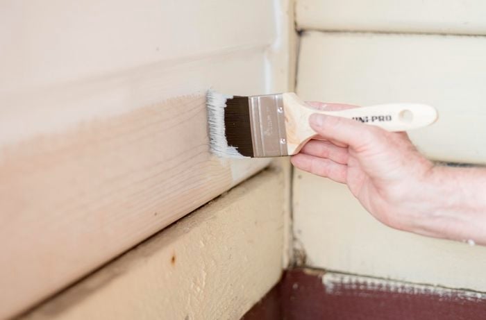 A person painting new weatherboards with primer