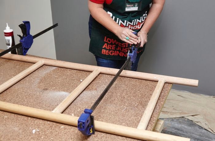 Person clamping both sides of wooden ladder together to hold it tight while glue dries.