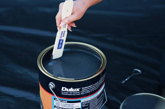 A person is mixing exterior fence paint before spray painting​​