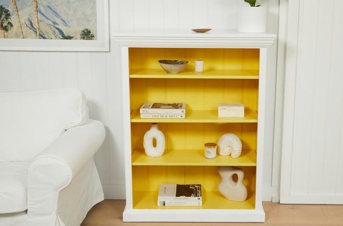 An upcycled yellow and white bookcase with accessories on it.