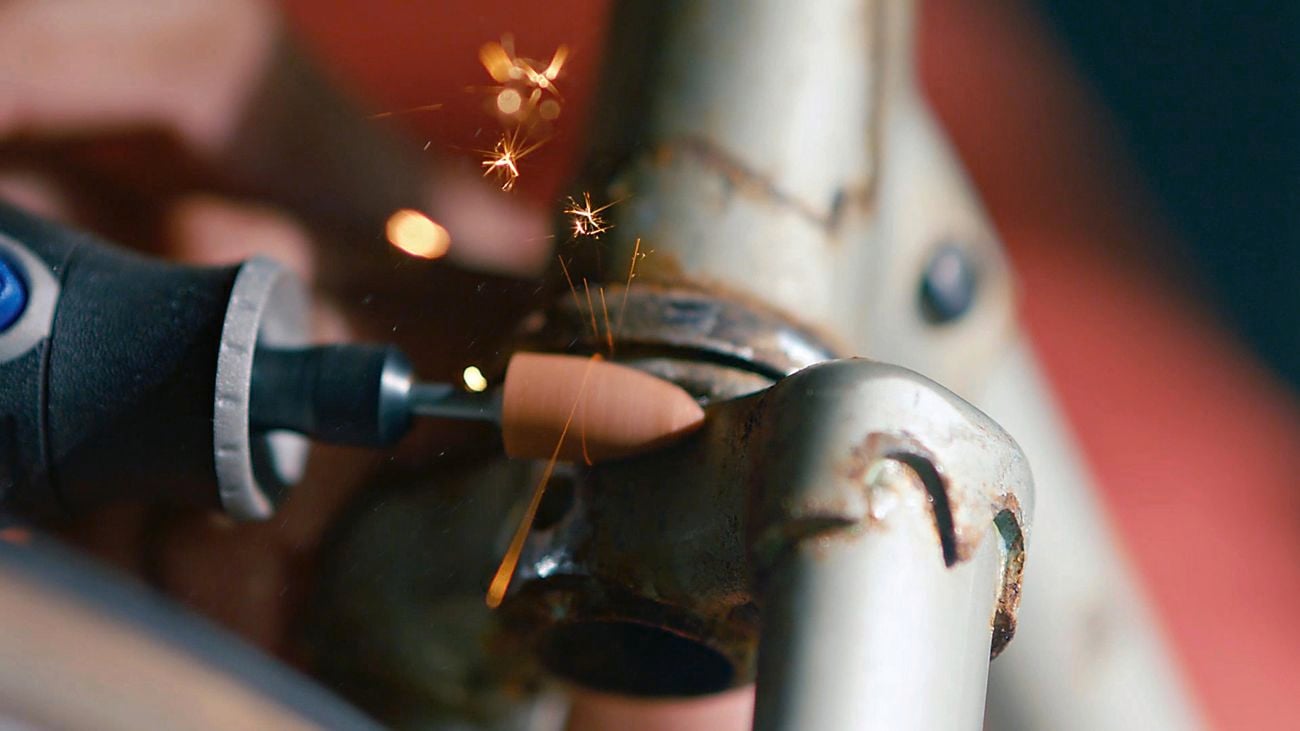 A person using a Dremel rotary tool to remove rust off metal pipes.