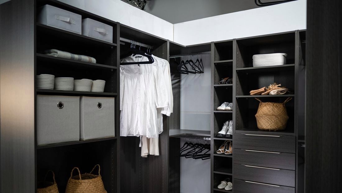 Walk in wardrobe with drawers, shelves, clothes hanging on coat hangers and shoes.