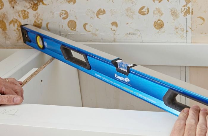A spirit level being used to ensure an installed kitchen cabinet is square to the wall