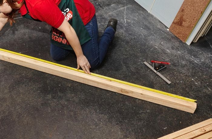 Person using measuring tape to measure length of timber lying on the ground.