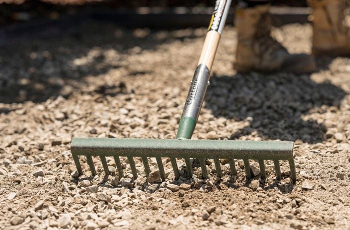 A close up of a metal rake being used to spread the road base evenly across the area.  ] 