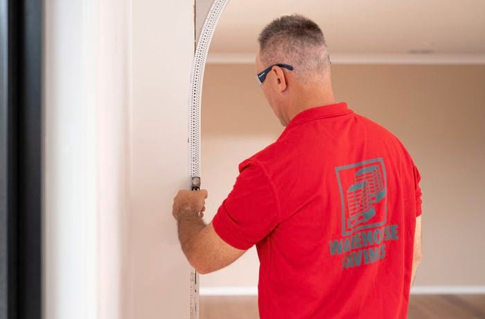 A Bunnings Team Member is installing a flexible plastic external moulding along the edge of a plaster archway.