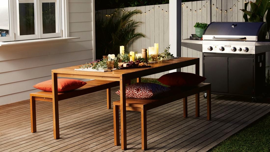 Outdoor dining table set with candles, greenery and cheese board with BBQ in the background.