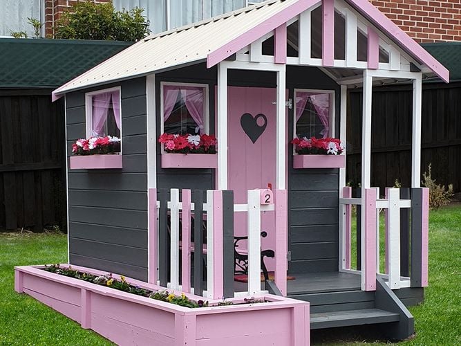 Children's playhouse painted pink and grey with decorated door, windows and flower boxes