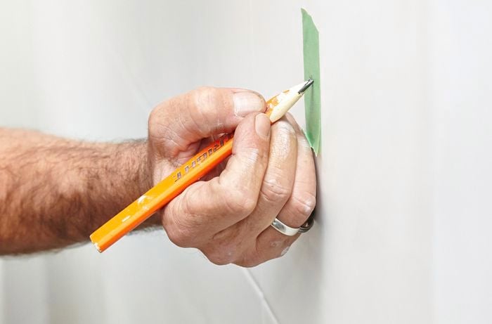 A person making a mark with a pencil on masking tape on a tile wall