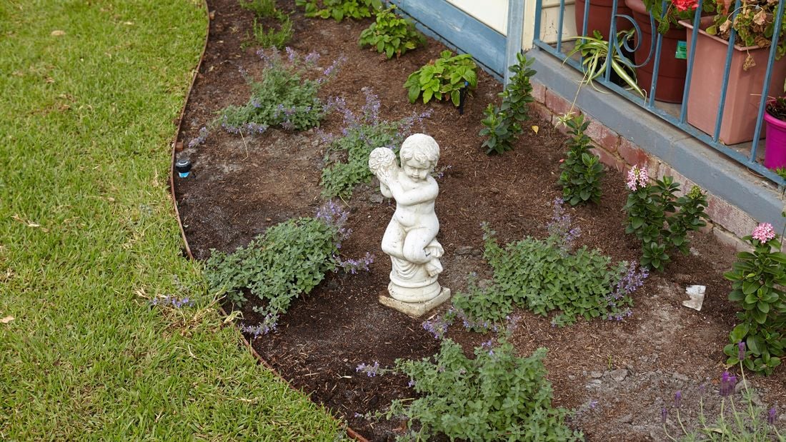 A small statue in a curved garden bed with new plants