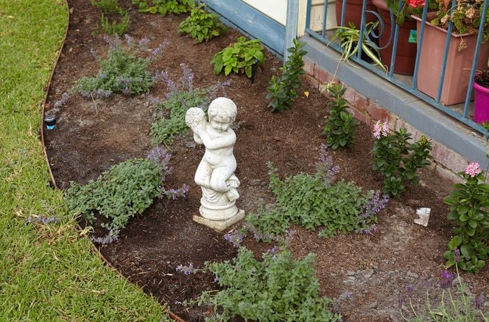 A small statue in a curved garden bed with new plants