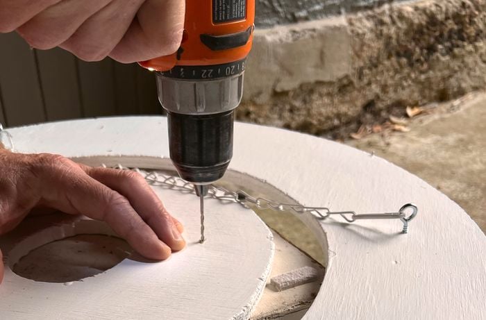 A person pre-drilling holes into plywood frames and installing screw eyes