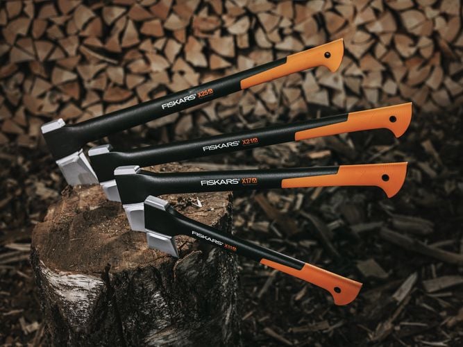 Several axes embedded in a log in front of a wall of chopped firewood