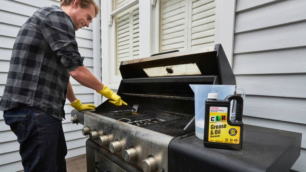 A man cleaning a barbecue with CLR Grease & Oil Remover