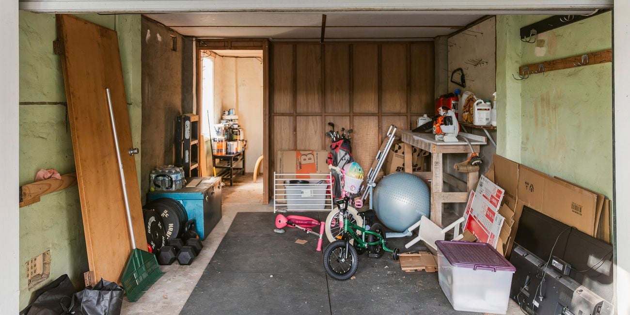Before view of a cluttered garage with scattered storage items, kids’ bikes and equipment.