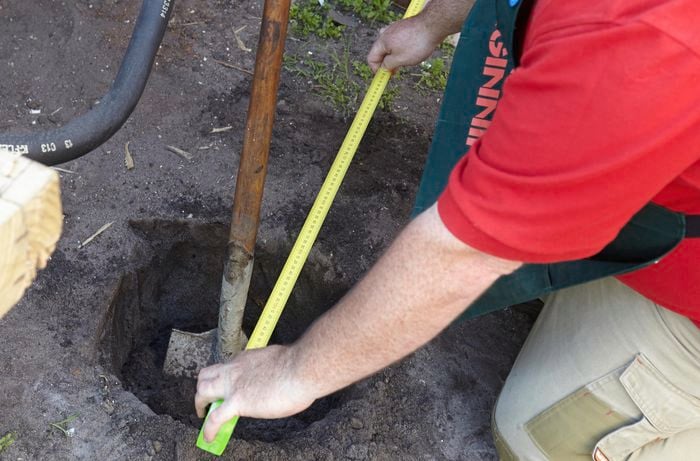Person using measuring tape to determine how big the hole is they just dug.
