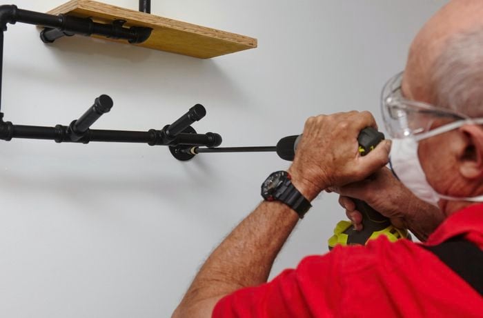 An ironing board storage rack being mounted to the wall with a power drill