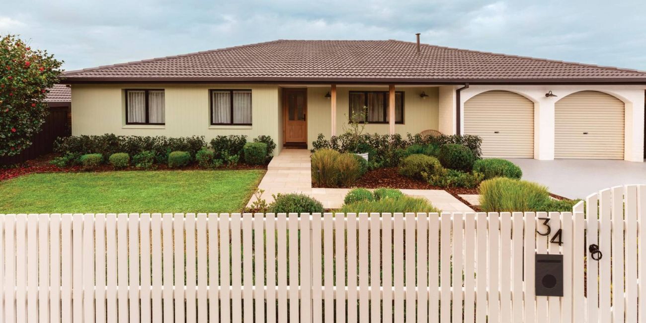 front of a house with picket fence and lush garden