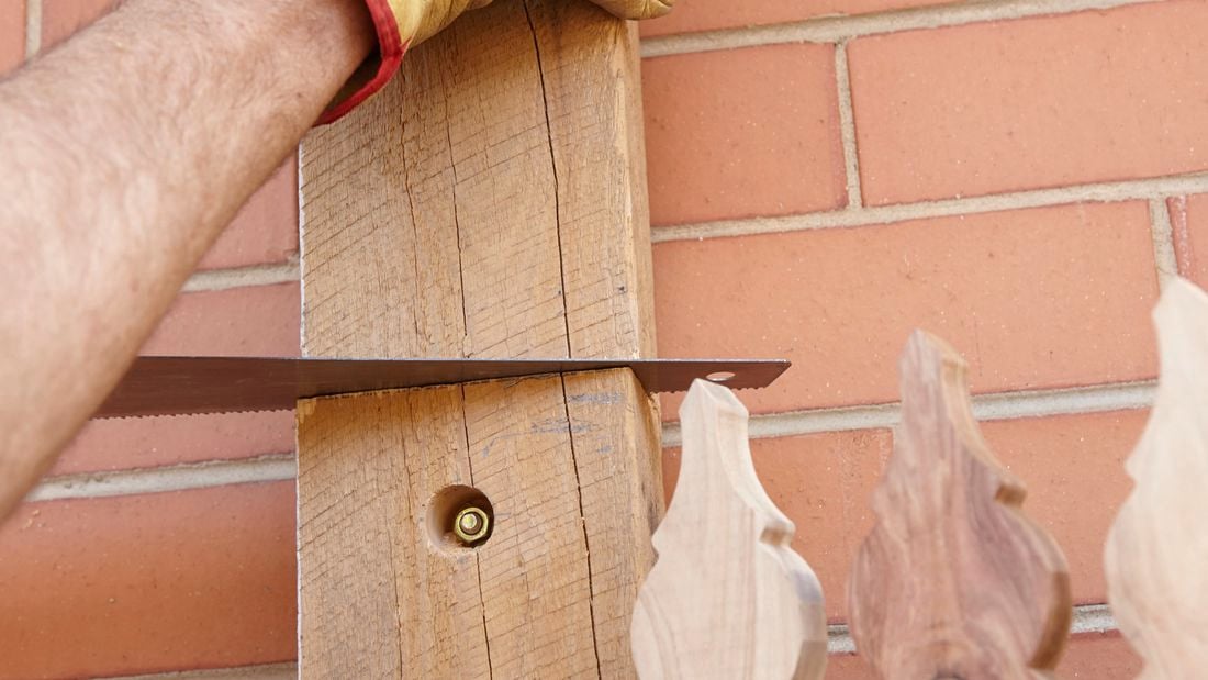 A person sawing a timber post bolted to a brick wall