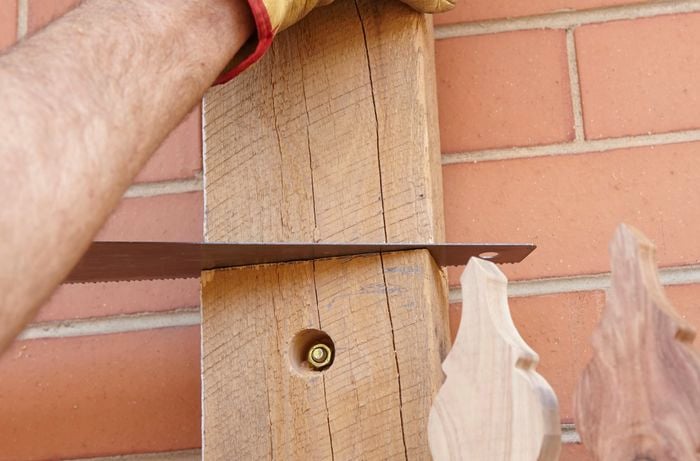 A person sawing a timber post bolted to a brick wall
