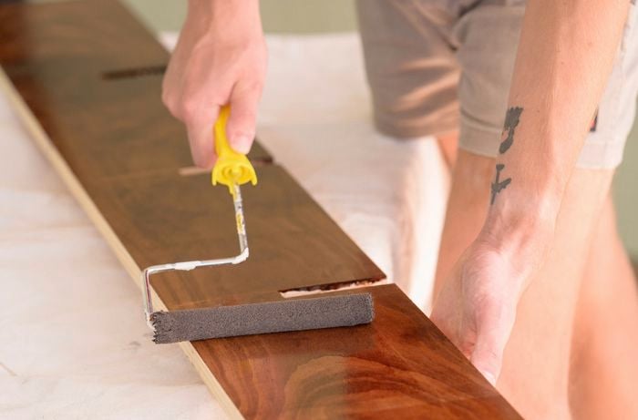 A person is using a foam roller to apply a paint or varnish to a wooden panel.