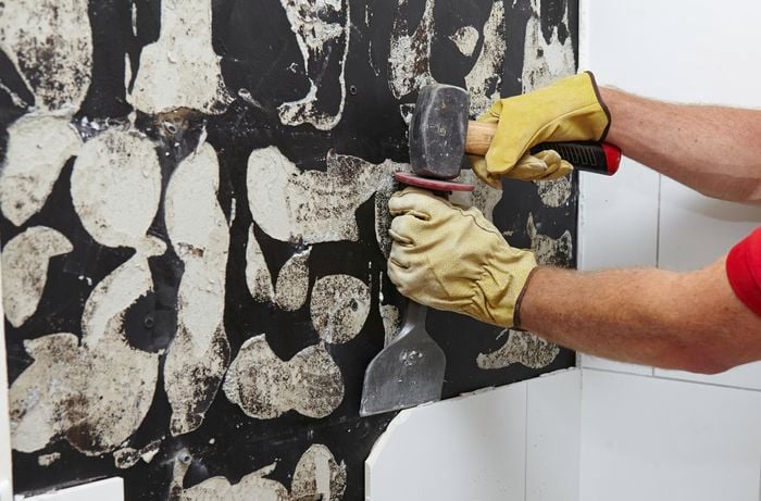 A Bunnings team member removing tiles from a wall with a mash hammer and brick bolster