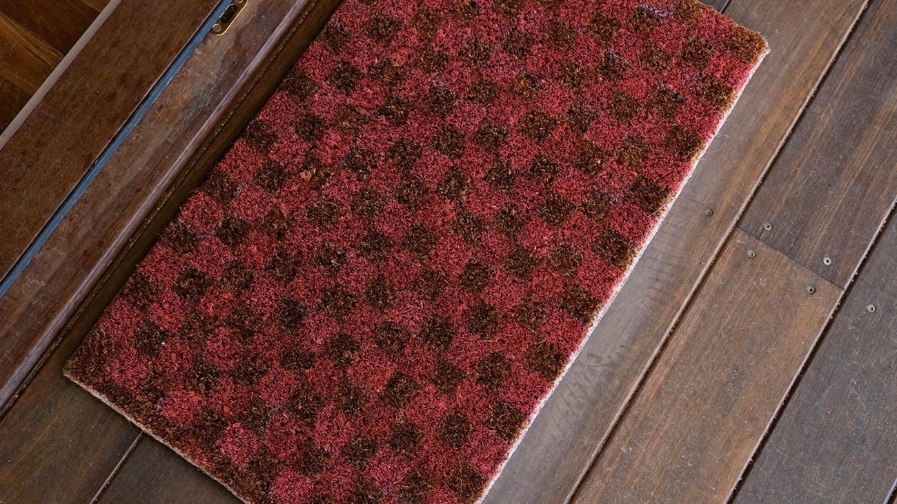 Checkered, red doormat next to white, cowboy boots on top of  hardwood floor.