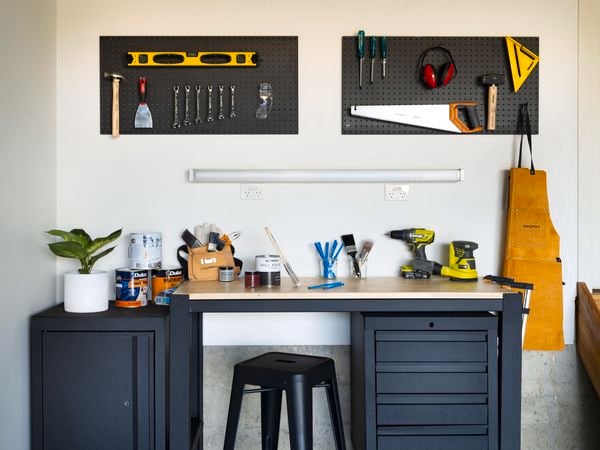 A black workbench with timber benchtop, a matching lockable cabinet and small tools hung on a black pegboard