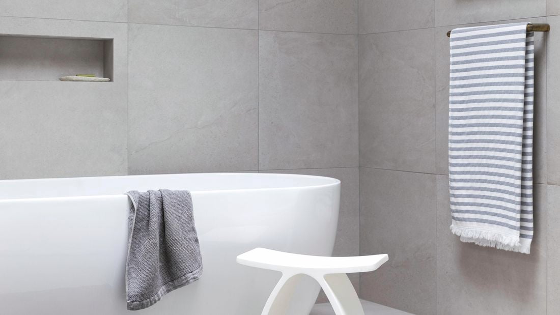 Modern, white bathtub in bathroom with gray and white tiles.