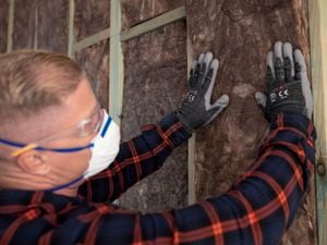 A man with eye protection, gloves and a mask installs Earthwool Insulation into a wall cavity