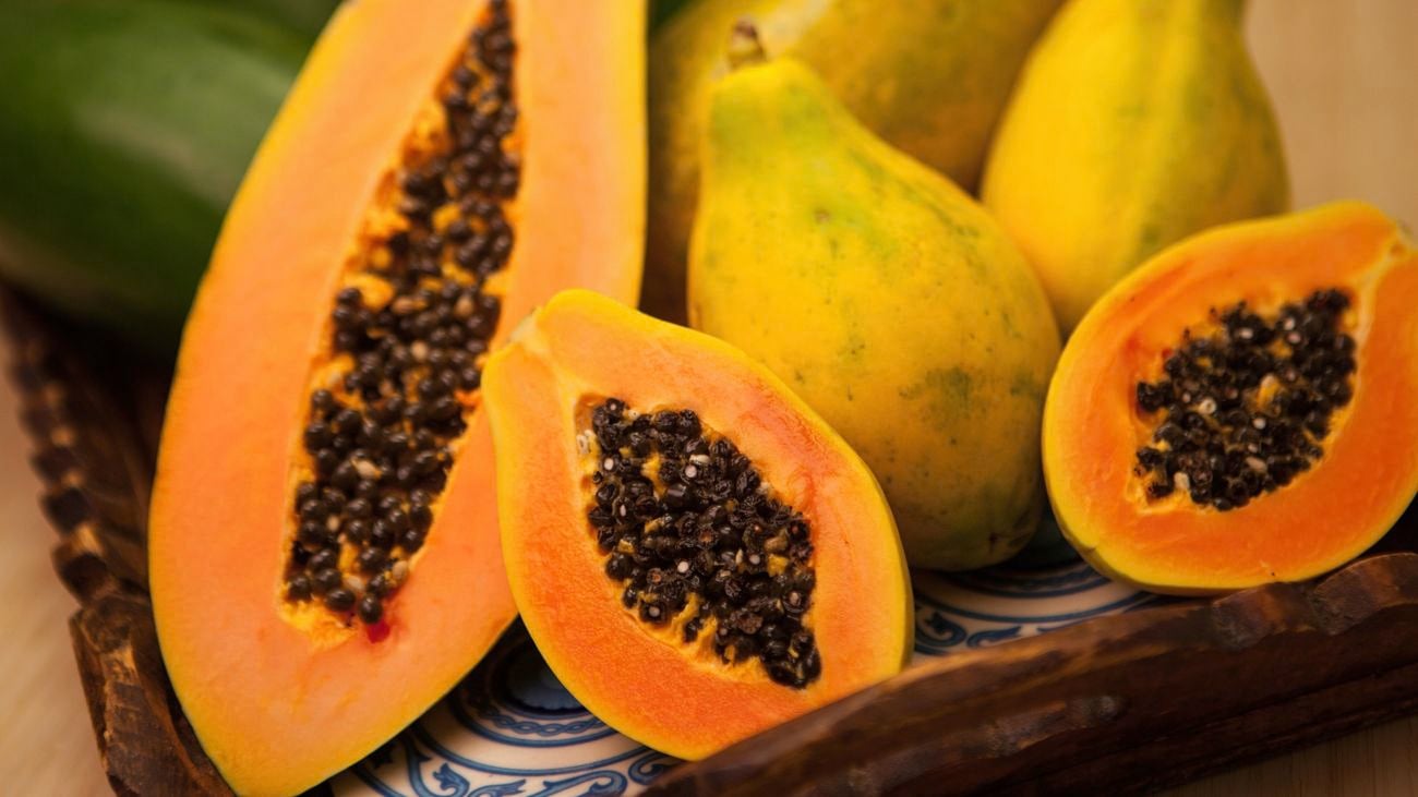 A group of papaya on a serving tray with bright orange fruit and green-and-yellow skin. A few are halved, showing black seeds in the middle of the fruit