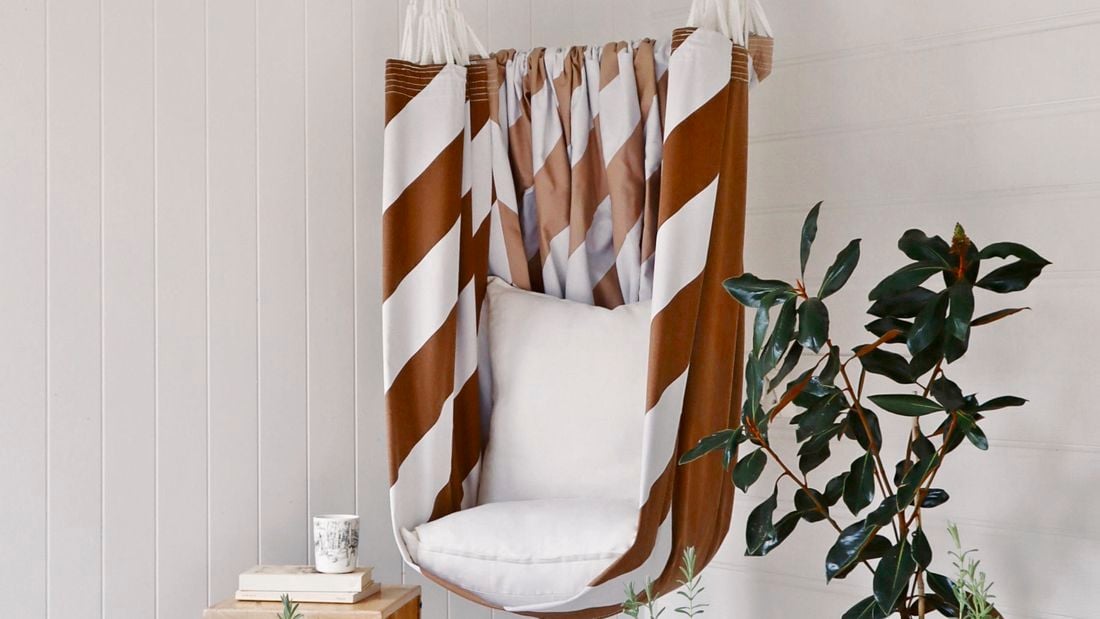 Brown and white striped hammock chair hanging in a white painted undercover area
