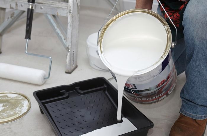 A person pouring paint into a roller tray