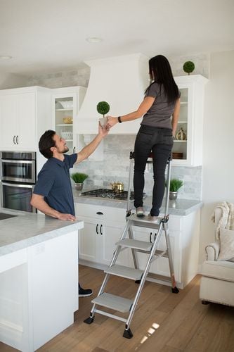 Woman standing on ladder decorating kitchen with indoor plants