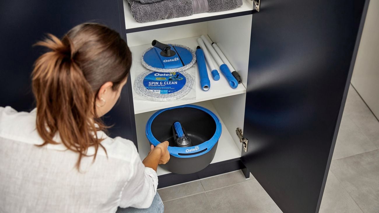 Person storing their folded down spin mop and bucket in cupboard.