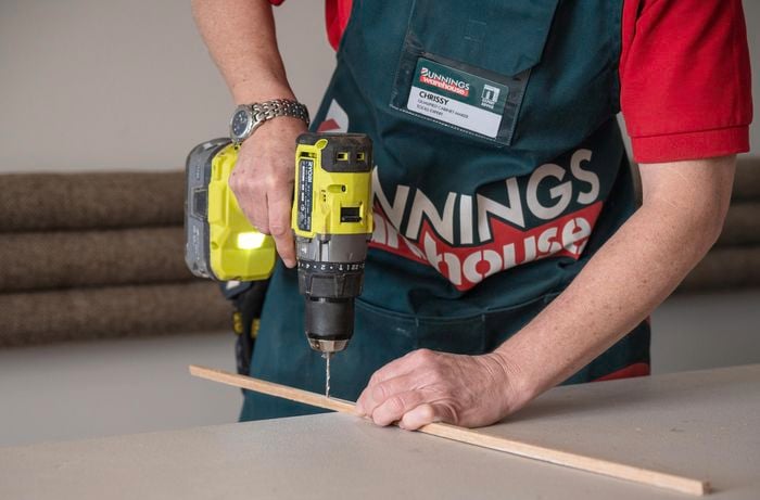 A person drilling the wood trim using a drill bit.