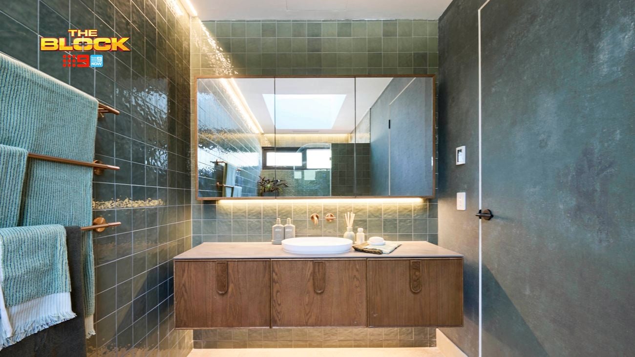 Modern bathroom with green tiled walls, floating wood vanity, and large mirror.