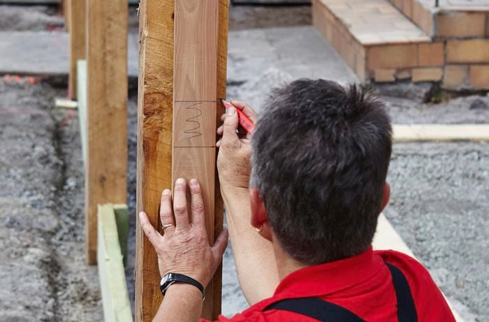 A person marking a fence post using a picket for reference