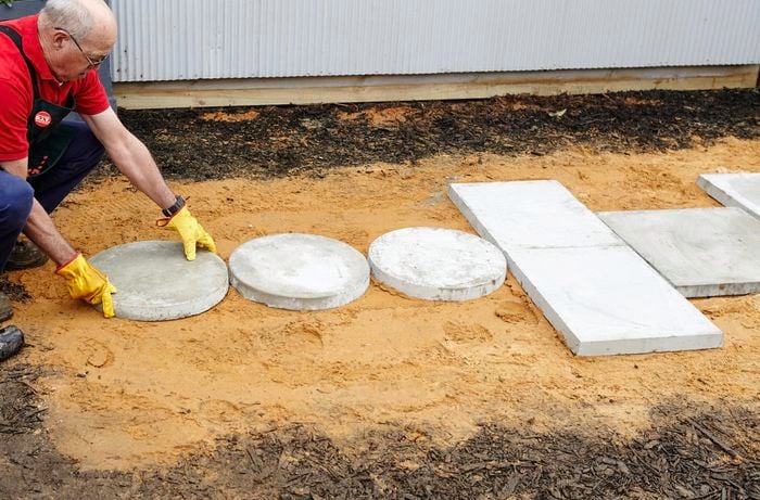 Man laying a round concrete paver on sand base